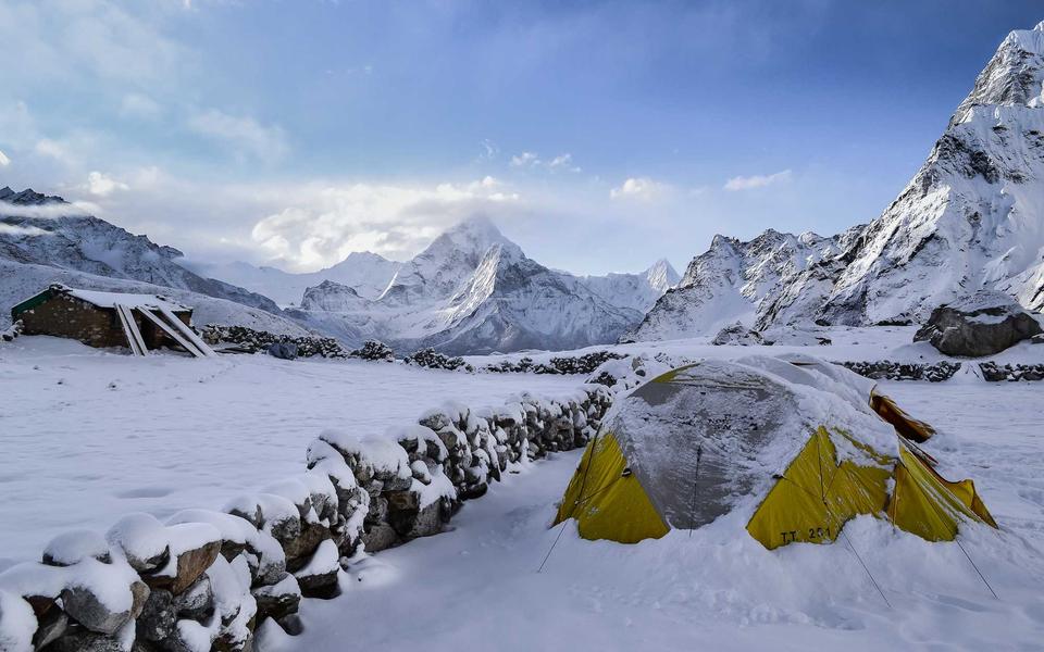 Yellow tents half buried in snow at a camp, with snowy peaks behind